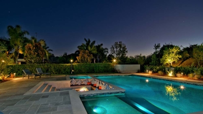Illuminated pool at night with sunken firepit seating area Photo