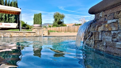 Covered bench swing next to pool with waterfall and fire features. Photo