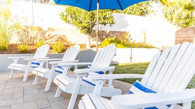 White Adridondack chairs surrounding a backyard pool oasis. Photo