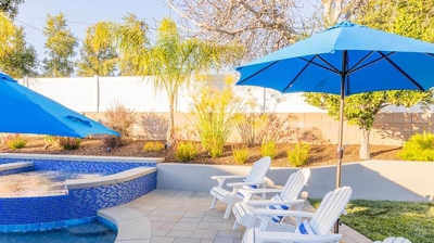 Relax in style with a backyard pool showcasing blue tile decor, umbrellas for shade, and white chairs. Photo