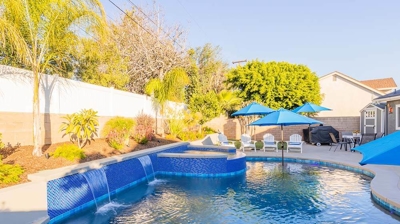 In the backyard, a pool with blue tile detailing and umbrellas, accompanied by an above-ground spa. Photo