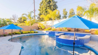 An outdoor haven with a pool featuring blue tiles, shaded by umbrellas, and enhanced by an above-ground spa. Photo