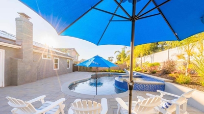 Backyard bliss awaits with a pool accented by blue tiles, surrounded by umbrellas, and complete with an above-ground spa. Photo