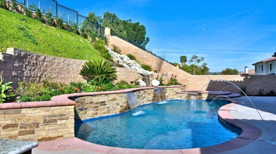 Swimming pool with water features next to a high retaining wall with landscaping. Photo