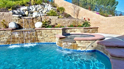 A stone-laden backyard retreat featuring a tranquil pool and cascading water features. Photo