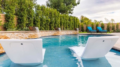 An idyllic backyard haven with a swimming pool and lounge chairs amidst verdant hedges. Photo
