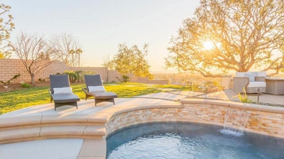 A charming backyard haven with a pool, foliage, fire pit, and inviting seating. Photo