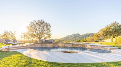 A serene backyard oasis with a pool, lush grass, fire pit, and comfy seating. Photo