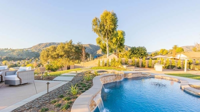 A stunning backyard oasis with a pool amidst lush greenery, paired with a fire pit and comfy seating. Photo