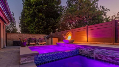 A long rectangular pool with built-in spa next to a fire feature with ample seating in the area. Photo