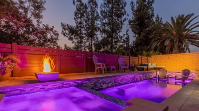 An extensive pool with a built-in spa, near a fire feature and generous seating, lit with pink pool lights. Photo