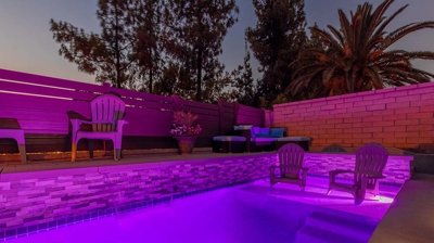A large rectangular pool with plenty of seating available nearby and pinkish purple hues lighting the pool. Photo