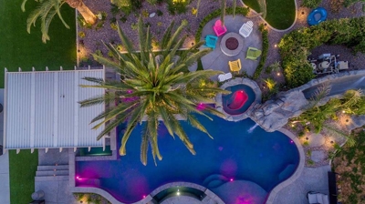 Aerial view of blue lit pool and patio alongside a serene view of landscaping. Photo
