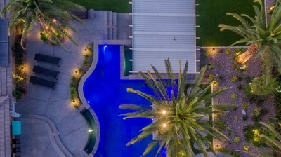 Aerial view of blue lit pool and patio alongside a serene view of landscaping. Photo