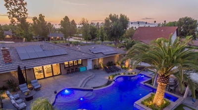 Aerial view of blue lit pool and patio alongside a serene view of landscaping. Photo