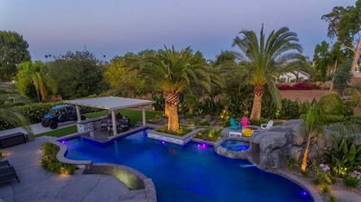 Aerial view of blue lit pool and patio alongside a serene view. Photo