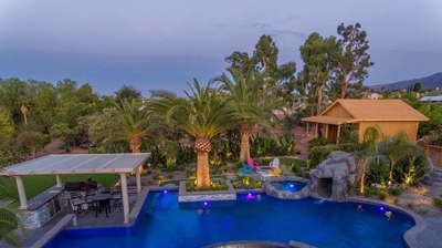Aerial view of blue lit pool and patio alongside a serene view. Photo
