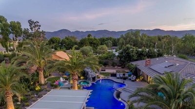 Aerial view of blue lit pool and patio alongside a serene view of mountains. Photo