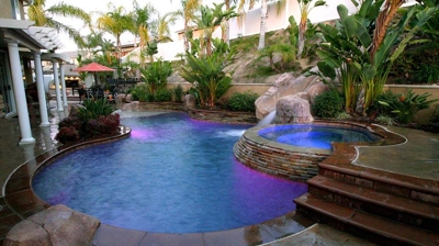 Lit up outdoor pool and jacuzzi with a serene green view. Photo