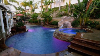 Outdoor pool and jacuzzi lit up with beautiful stone flooring. Photo