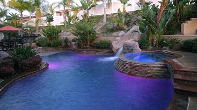 Outdoor pool and jacuzzi lit up with beautiful stone flooring. Photo