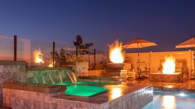 Stunning backyard retreat: pool, elevated spa, waterfall, and flickering fires. Photo