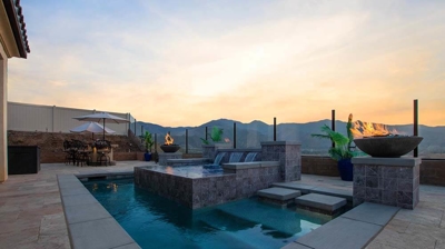 Tranquil backyard paradise: pool, spa above, waterfall, and fiery accents. Photo