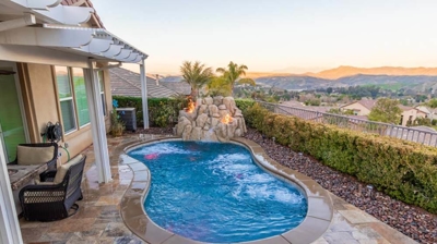 Retreat-like backyard escape showcasing a pool surrounded by hedges, complemented by a rock waterfall with fire features. Photo