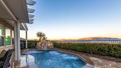 Backyard sanctuary with a pool with hedges, featuring a rock waterfall and accentuated by fire.. Photo