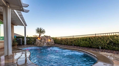 Luxurious hedged backyard pool oasis with cascading rock waterfall and mesmerizing fire accents. Photo