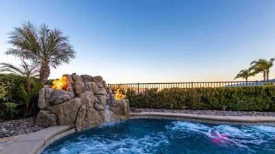 Tranquil backyard haven complete with a hedged-in pool, rock waterfall, and fire-enhanced ambiance. Photo