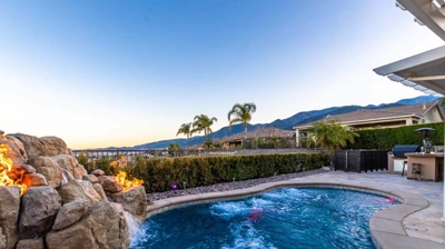 A pool bordered by hedges, accented with a rock waterfall and fiery touches. Photo
