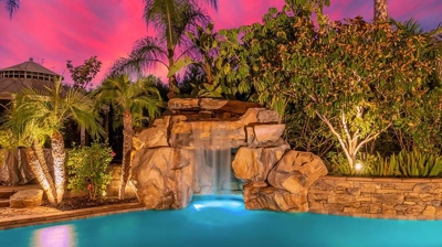 Lush backyard oasis encircled by palm trees and a rock waterfall going into the pool. Photo