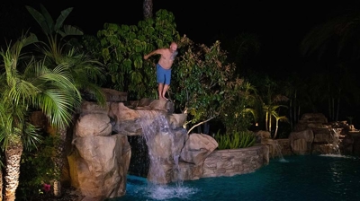 A man jumps off of the rock waterfall into the pool below at night. Photo