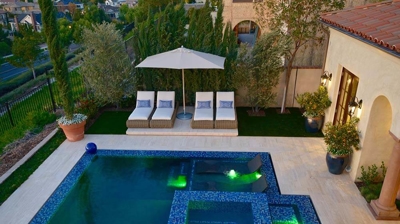 Lit up pool with lawn chairs and umbrella. Photo