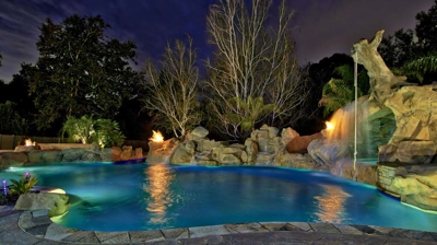 Custom freeform pool at night with fire features and rope swing Photo