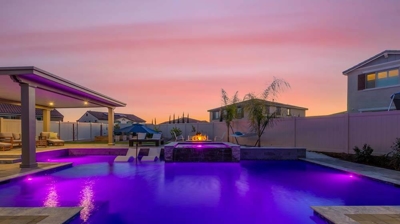 Square-like pool lit in purple lighting within sunset of home backyard Photo
