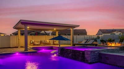 Square-like pool lit in purple lighting featuring a patio section for lounging Photo