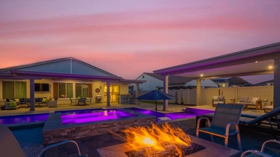 Purple lighting coming from modern pool alongside a cozy outdoor fireplace Photo