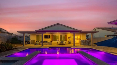 A lit up home in the background with modern purple lights coming from pool Photo