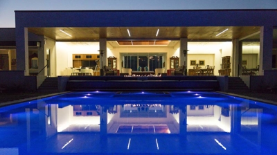 A posh sanctuary at night with a view into the home and a spacious swimming pool. Photo