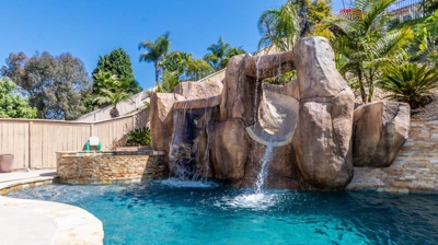 An enchanting outdoor space with a pool, hot tub, and stunning waterfall feature Photo