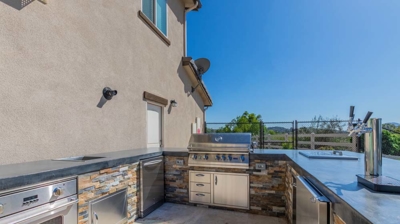 Sunny outdoor kitchen area complete with a grill, oven, and taps for cooking and cleaning Photo