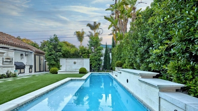 Large rectangular pool in backyard with trees on the right Photo