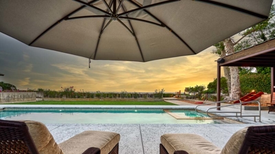 The view of a pool and a sunset from lounge chairs Photo