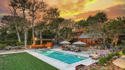 A view of a large backyard with trees and a pool with lounge chairs behind it Photo