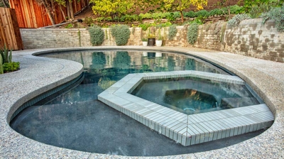 View of curvy pool with built in jacuzzi in the backyard Photo