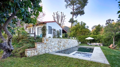 An in-ground pool built below a house with a stone retaining wall Photo