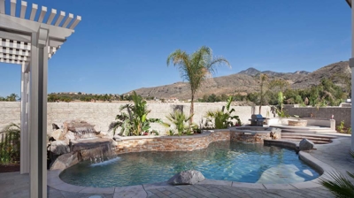 Desert pool sanctuary adorned with palm tree and spa featuring a calming waterfall. Photo
