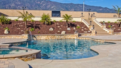 Winding pool situated outdoors with a spa and a landscaped hill next to a wall. Photo
